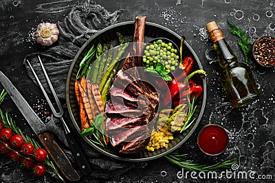 Grilled steak on the bone with grilled vegetables. On a black background. Top view. Free copy space Stock Photo