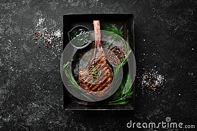Grilled steak on the bone. Tomahawk steak on a black stone background. Top view. Free copy space Stock Photo