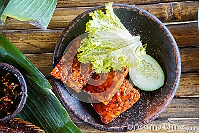 Grilled tempeh or fried tempeh with red barbecue sauce, vegetables and chili sauce served on an earthenware mortar Stock Photo