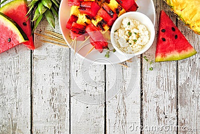 Grilled summer watermelon and pineapple fruit kabobs, overhead view top border on white wood Stock Photo
