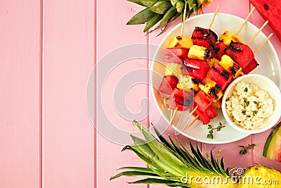 Grilled summer watermelon and pineapple fruit kabobs, top view side border on a pink wood background Stock Photo
