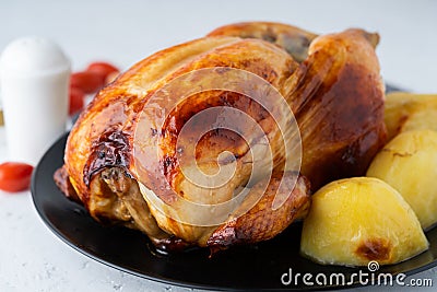 Grilled whole chicken in black plate on white table, baked meat with potatoes. Side view, close up Stock Photo