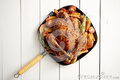 Grilled whole chicken in cast iron black pan with potatoes, tomatos and rosemary Stock Photo