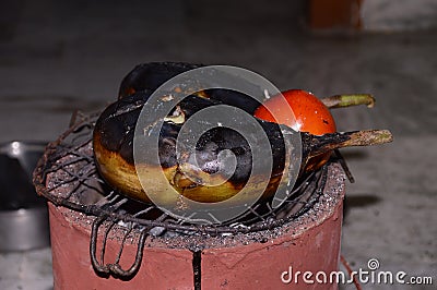 Grilling of Brinjal and tomato on coal stove or charcoal stove or mitti ka chulha or charcoal chulha or coal chulha or charcoal Stock Photo