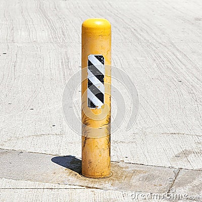 Gritty Yellow Safety Bollard on Concrete Pavement Stock Photo