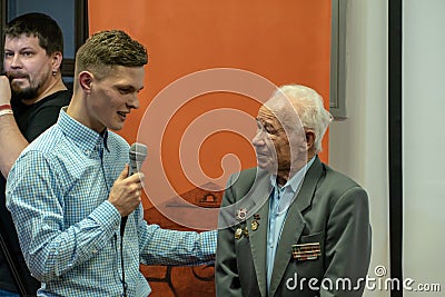 Grodno, Belarus, January 16, 2019: A young reporter holding a microphone. Conversation with an elderly man on stage. The retiree Editorial Stock Photo