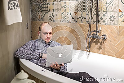 GRODNO, BELARUS - MARCH 2019: young man employees lays in bath with notebook computer in modern luxury plumbing store Editorial Stock Photo