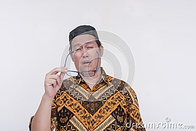 A groggy and stressed middle aged man takes off his glasses after feeling eyestrain. An overworked person wearing a batik shirt Stock Photo