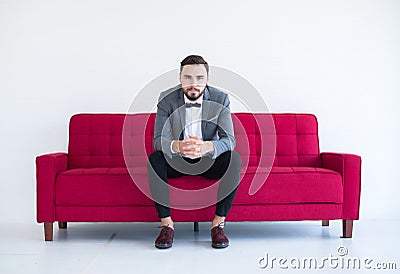 Groom with bearded sitting on sofa red and smiling in formal tuxedo and suit in wedding day on white background,Copy space for tex Stock Photo