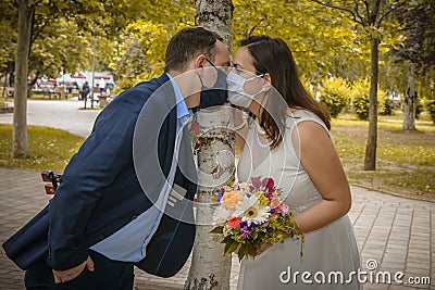 Groom and bride kissing each other in protective medical masks on face in Stock Photo