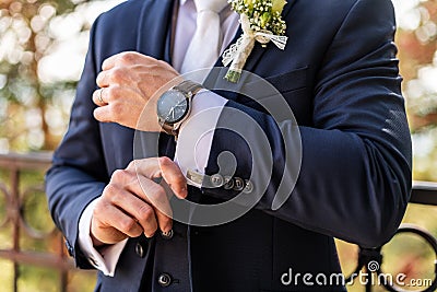Groom fixing his cufflinks. Handsome groom dressed in dark blue formal suit getting ready for wedding. Elegant groom. Stock Photo