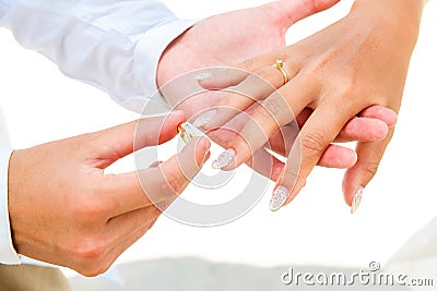 Groom giving an engagement ring to his bride under the arch decorated with flowers on the sandy beach. Wedding ceremony on Stock Photo