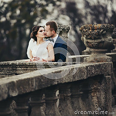 Groom kisses a bride hugging her from behind on the old balcony Stock Photo