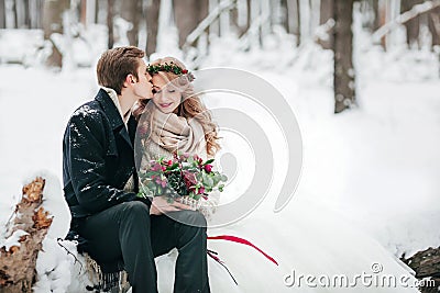 Groom is kissing his bride on the temple on background of the snowy forest. Winter wedding. Artwork Stock Photo