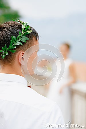 The groom in an olive wreath and a white shirt, in front of a silhouette of the bride in defocus Stock Photo