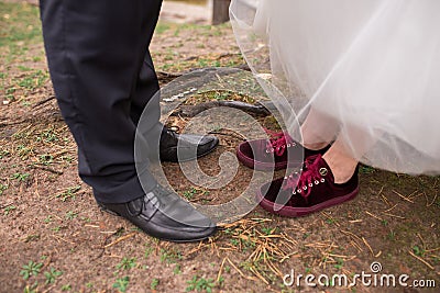 The groom in trousers and black shoes and the bride in red sneakers showing their wedding shoes. Stock Photo