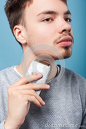 Grooming and skin care. Portrait of attentive focused brunette man removing facial hair. isolated on blue background Stock Photo