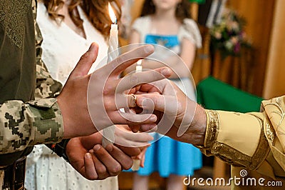 Grooms wear their wedding rings on their fingers. Groom in military uniform. The priest puts on a wedding ring. Stock Photo