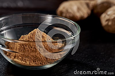 Ground ginger in a plate on a black background. In the background, the root of ginger. side view. sharp powder. macro photo. Stock Photo