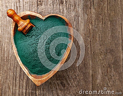 Ground Spirulina in bowl on wood background, top view on heart shape dish with superfood Stock Photo