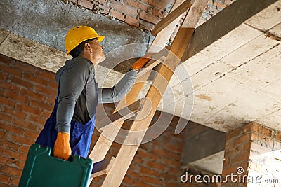 From the ground up. Young male builder in blue overalls and hard hat climbing up the ladder, holding toolbox while Stock Photo