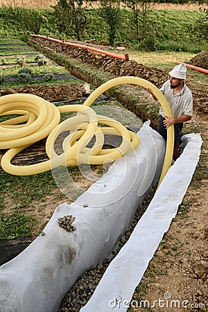 A worker carries a yellow perforated drainage pipe. Groundwater drainage works in the field Stock Photo