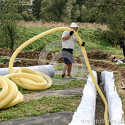 A worker carries a yellow perforated drainage pipe. Groundwater drainage works in the field Stock Photo