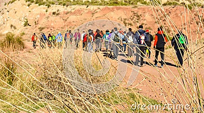group of adult people with colorful backpack trekking on a path of sand and stones walking to mountain with a amazing landscape on Editorial Stock Photo