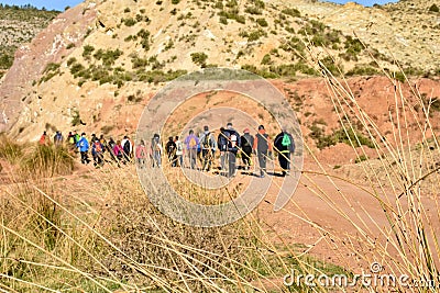group of adult people with colorful backpack trekking on a path of sand and stones walking to mountain with a amazing landscape on Editorial Stock Photo