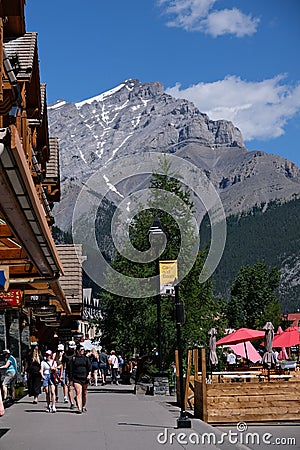 Group of adults walking down a street with towering mountains in the background, Banff Alberta Editorial Stock Photo