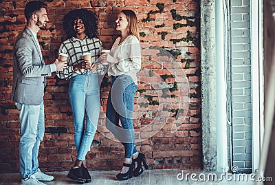 Group of attractive business people, standing next to each other, holding a cups, smiling standing at the brick wall Stock Photo