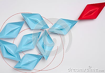 Group of blue paper boats heading in one direction and one red one heading in the opposite direction Stock Photo