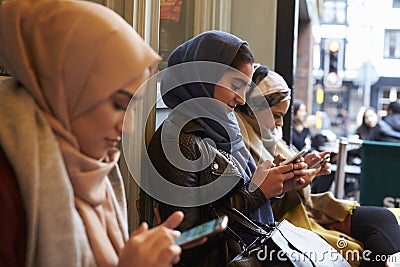 Group Of British Muslim Women Texting Outside Coffee Shop Stock Photo