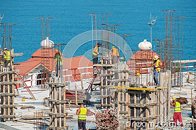 Group of building workers working on the top of the construction site with blue sea background Editorial Stock Photo