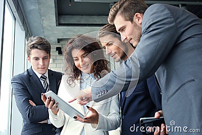 Group of businesspeople using a digital tablet together in front of office windows. Stock Photo