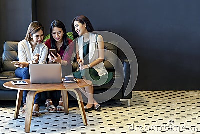 Group of charming beautiful Asian women using smartphone and laptop, chatting on sofa at cafe, modern lifestyle Stock Photo