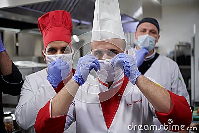 Group chefs standing together in the kitchen at restaurant wearing protective medical mask and gloves in coronavirus new normal Stock Photo