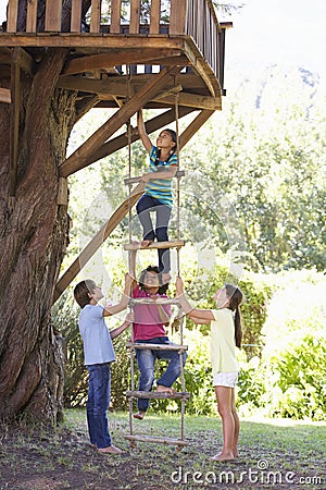 Group Of Children Climbing Rope Ladder To Treehouse Stock Photo