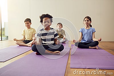 Group Of Children Sitting On Exercise Mats And Meditating In Yoga Studio Stock Photo