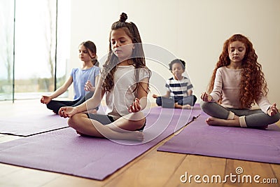 Group Of Children Sitting On Exercise Mats And Meditating In Yoga Studio Stock Photo