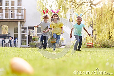 Group Of Children Wearing Bunny Ears Running On Easter Egg Hunt In Garden Stock Photo