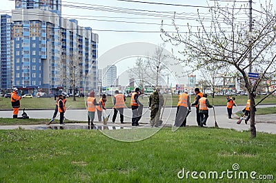 A group of cleaners of bright orange protective vests are sweeping the city sidewalk on a spring street in a residential area Editorial Stock Photo