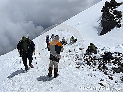 A group of climbers with backpacks and trekking poles stands and rests on a snowy trail Editorial Stock Photo