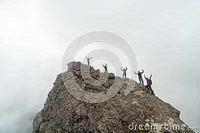 Group of climbers standing on a jagged mountain peak and waving their hands in the air Stock Photo