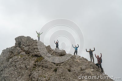 Group of climbers standing on a jagged mountain peak and waving their hands in the air Stock Photo