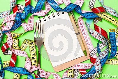 Group of colorful measure tapes, pen, open notebook and fork on green background with empty space for your idea. Top view of Stock Photo