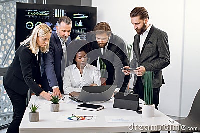 Group of confident high-skilled multiracial businesspeople, standing at the table and discussing business strategy Stock Photo