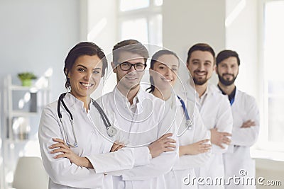 A group of confident practicing doctors in white coats are smiling against the backdrop of the clinic. Stock Photo