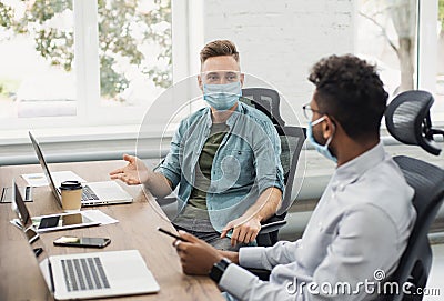 Group of coworkers people discussing business ideas while working in the office wearing medical protective face masks Stock Photo