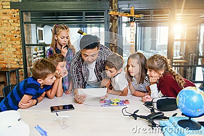 Group of curious school children listen their Korean male teacher uses device of tablet computer for show educational Stock Photo